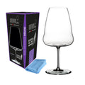 Das elegant gestaltete Weißweinglas Riedel Winewings Riesling mit hohem, dünnem Stiel wird neben seiner eleganten schwarz-violetten Geschenkverpackung präsentiert. Vor der Verpackung liegt ein hellblaues Poliertuch. Das Weinglas selbst hat einen breiten Kelch, der sich zum Rand hin sanft verjüngt.