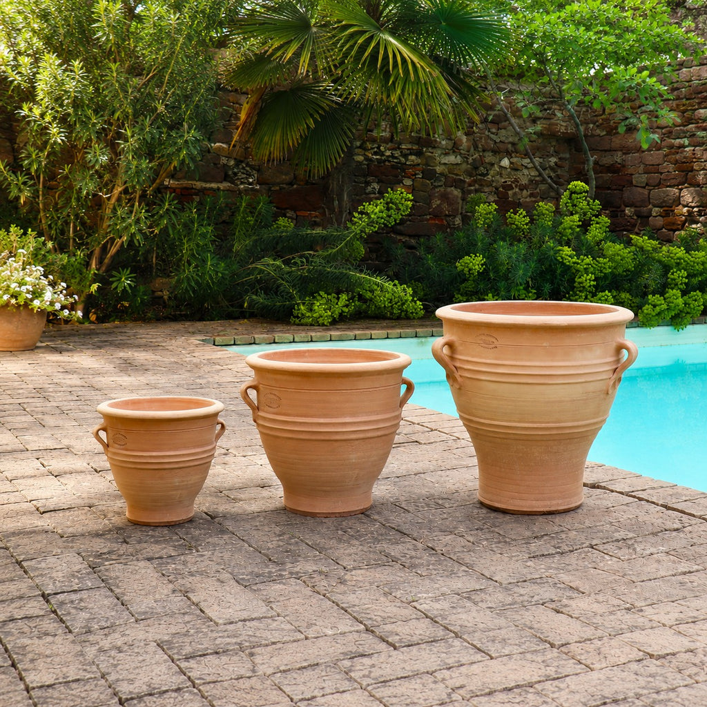 Ein winterhartes Terracotta Pflanzgefäß "Rosa", H=35 cm, steht auf einem Steinpatio neben dem Pool und ist von grünen Pflanzen und Bäumen umgeben.