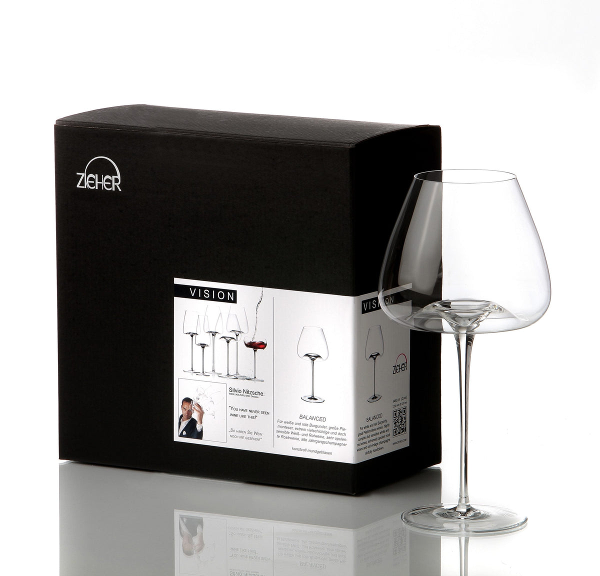 Eine schwarze Schachtel der Zieher Weinglas Balanced Vision-Serie - Mundgeblasenes Kristallglas XXL 850 ml steht neben einem einzelnen leeren Klarglas. Der Karton zeigt Produktbilder, Beschreibungen und das Branding auf einem weißen Etikett.