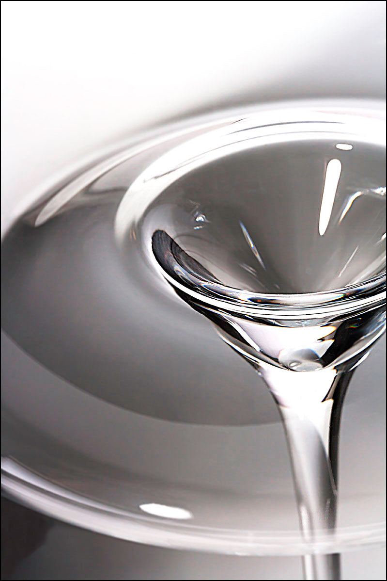 Nahaufnahme einer klaren Flüssigkeit, die in ein Zieher Weinglas Balanced Vision-Serie - mundgeblasenes Kristallglas XXL 850 ml gegossen wird. Dabei entstehen wirbelnde Reflexionen auf dem Kristallglas vor einem weiß-grauen Hintergrund.