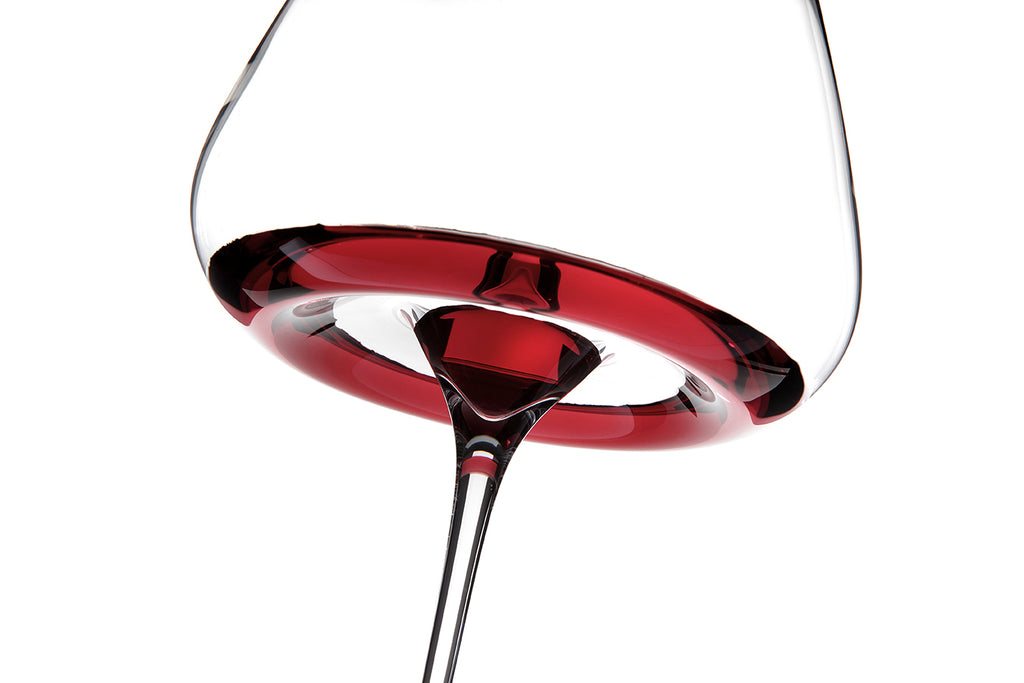Nahaufnahme von unten eines Zieher Weinglas Intense Vision-Serie, mundgeblasenes Kristallglas, teilweise mit Rotwein gefüllt, wobei die satte rote Flüssigkeit und der elegante Stiel vor weißem Hintergrund hervorgehoben werden.