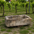 Das Waschbecken aus Sandstein 86 x 46 x 26 cm steht in einem üppigen Weinberg auf Kies vor lebendigen Weinstöcken, wobei grüne Blätter und gewundene Stämme einen malerischen Hintergrund bilden.