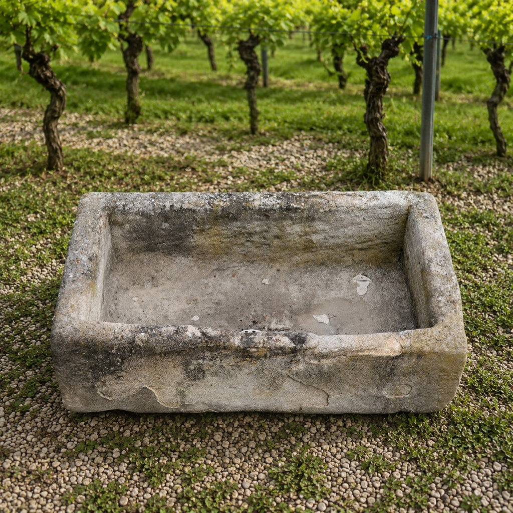 Ein Waschbecken aus Sandstein 86 x 46 x 26 cm ruht auf Kies vor Reihen von grünblättrigen Weinstöcken in einem Weinberg.
