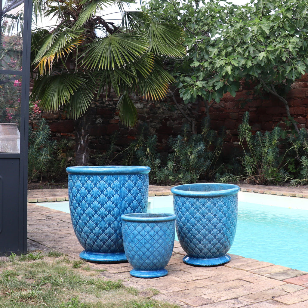 Drei "Azur Provence" türkis verglaste Blumentöpfe (30,5-54 cm hoch) stehen auf einer Backstein-Terrasse neben einem Pool, umgeben von Palmen und grüner Kulisse.