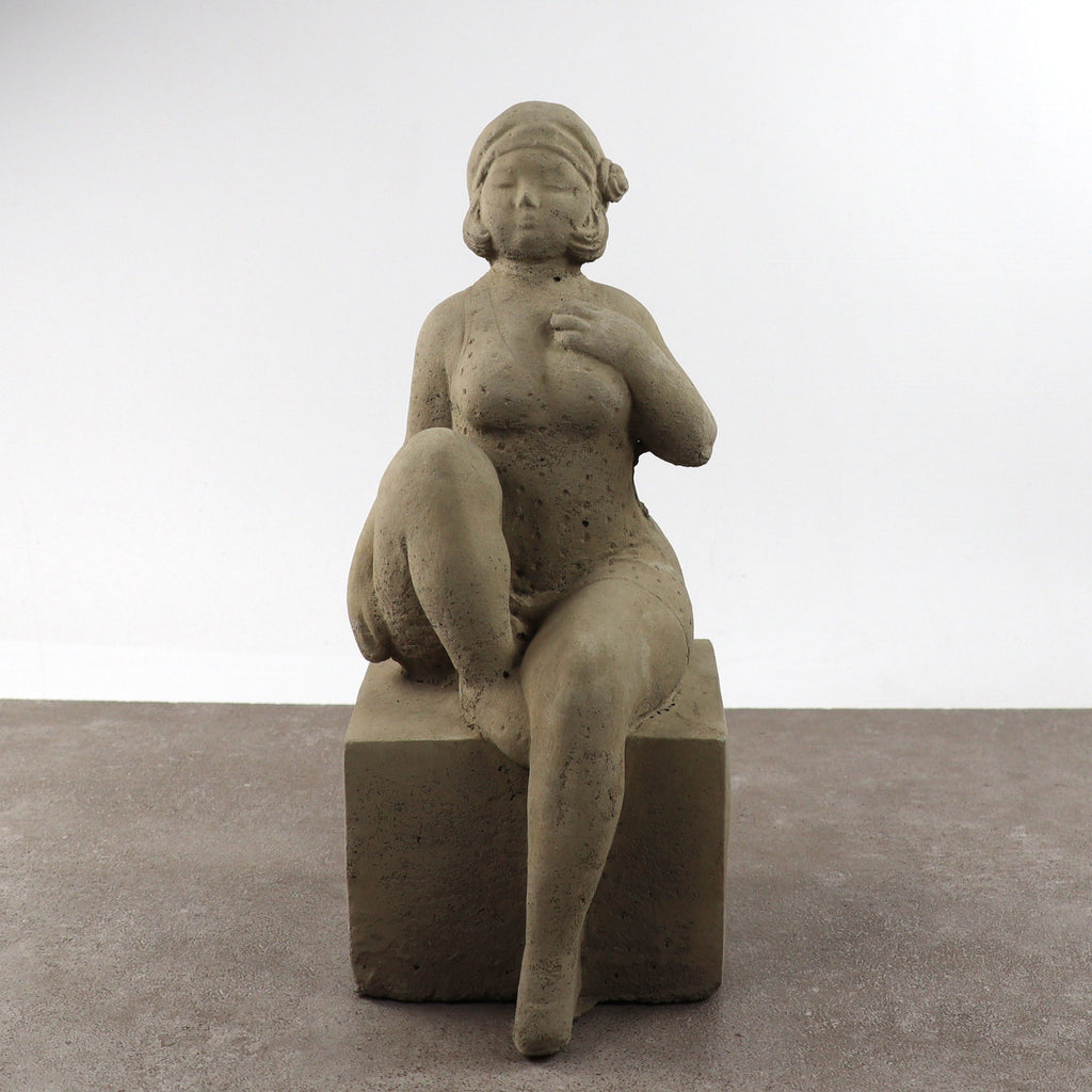 Die UV-beständige Gartenfigur "Badenixe" ist eine Steinskulptur einer sitzenden Frau mit erhobenem Knie auf einem quadratischen Block, die sich durch eine strukturierte Oberfläche und einen neutralen Ausdruck auszeichnet - eine elegante, dauerhafte Dekoration für jeden Außenbereich.