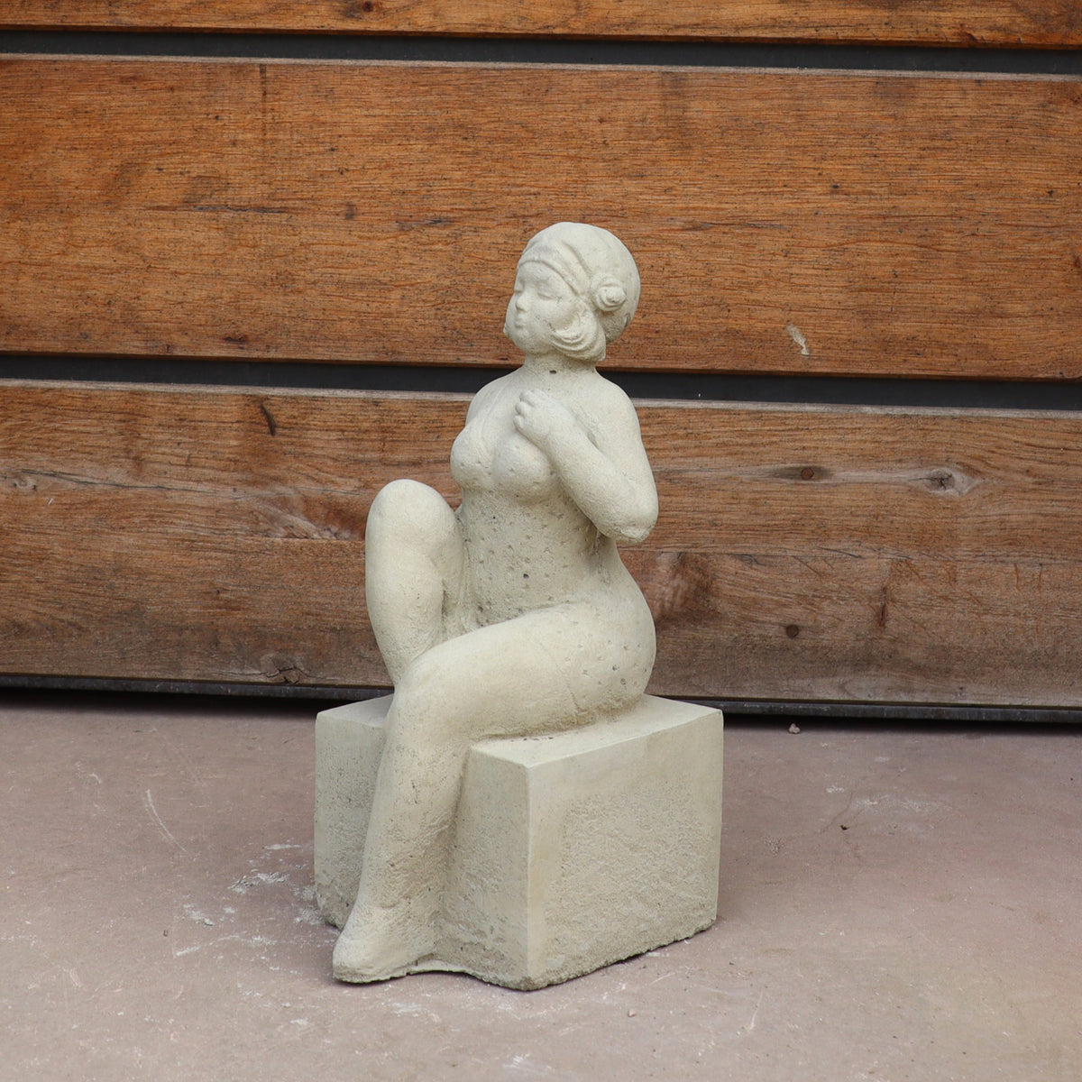 Die UV-beständige Gartenfigur "Badenixe" zeigt eine sitzende Frau mit kurzen, lockigen Haaren und erhobenem Knie auf einem Block - eine stilvolle Gartendekoration für Ihr Zuhause.