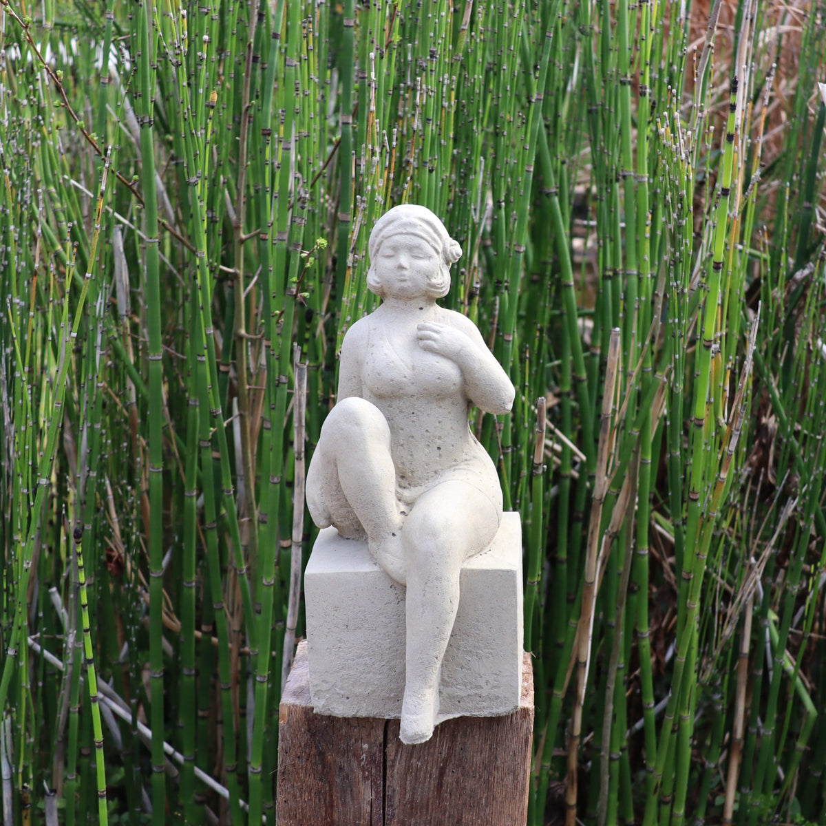 Die UV-beständige Gartenfigur "Badenixe": Eine elegante Frau sitzt als dekorative Statue auf einem hölzernen Pfosten.