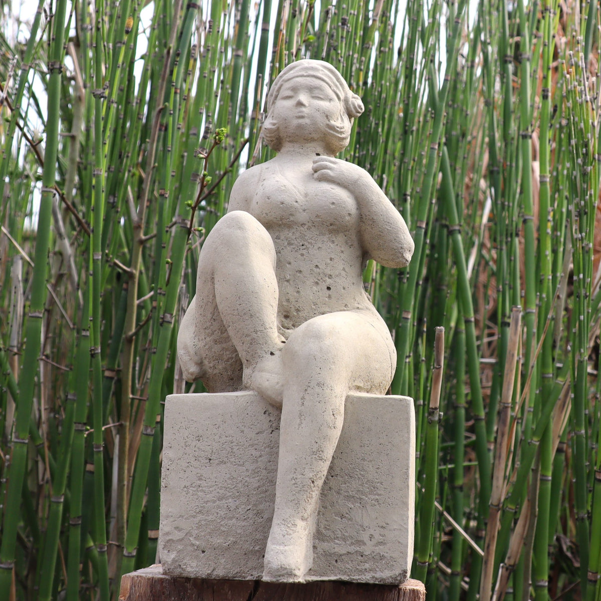 Die UV-beständige Gartenfigur "Badenixe" zeigt eine entspannte, teilweise unbekleidete Gestalt mit angezogenem Bein vor grünen Pflanzen und ist die perfekte, wetterfeste Dekoration für Ihren Garten.