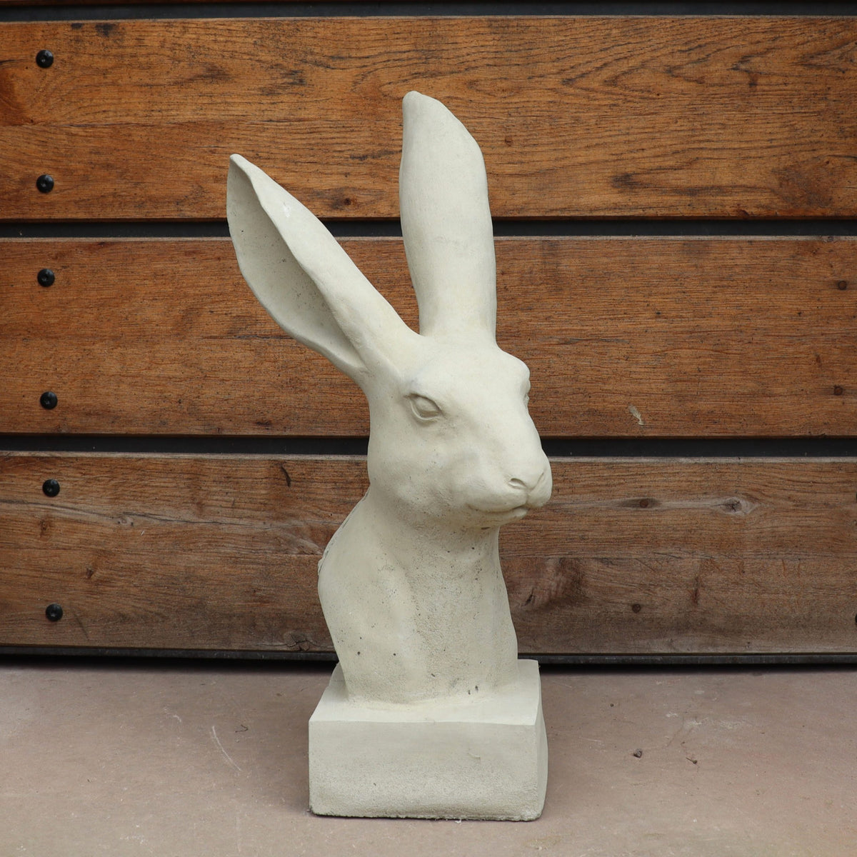Die handgefertigte Steinfigur "Hase" aus Deutschland zeigt einen beigen Hasenkopf mit langen Ohren auf quadratischem Sockel, präsentiert vor waagerechten Holzplanken und besticht durch hochwertige Verarbeitung.