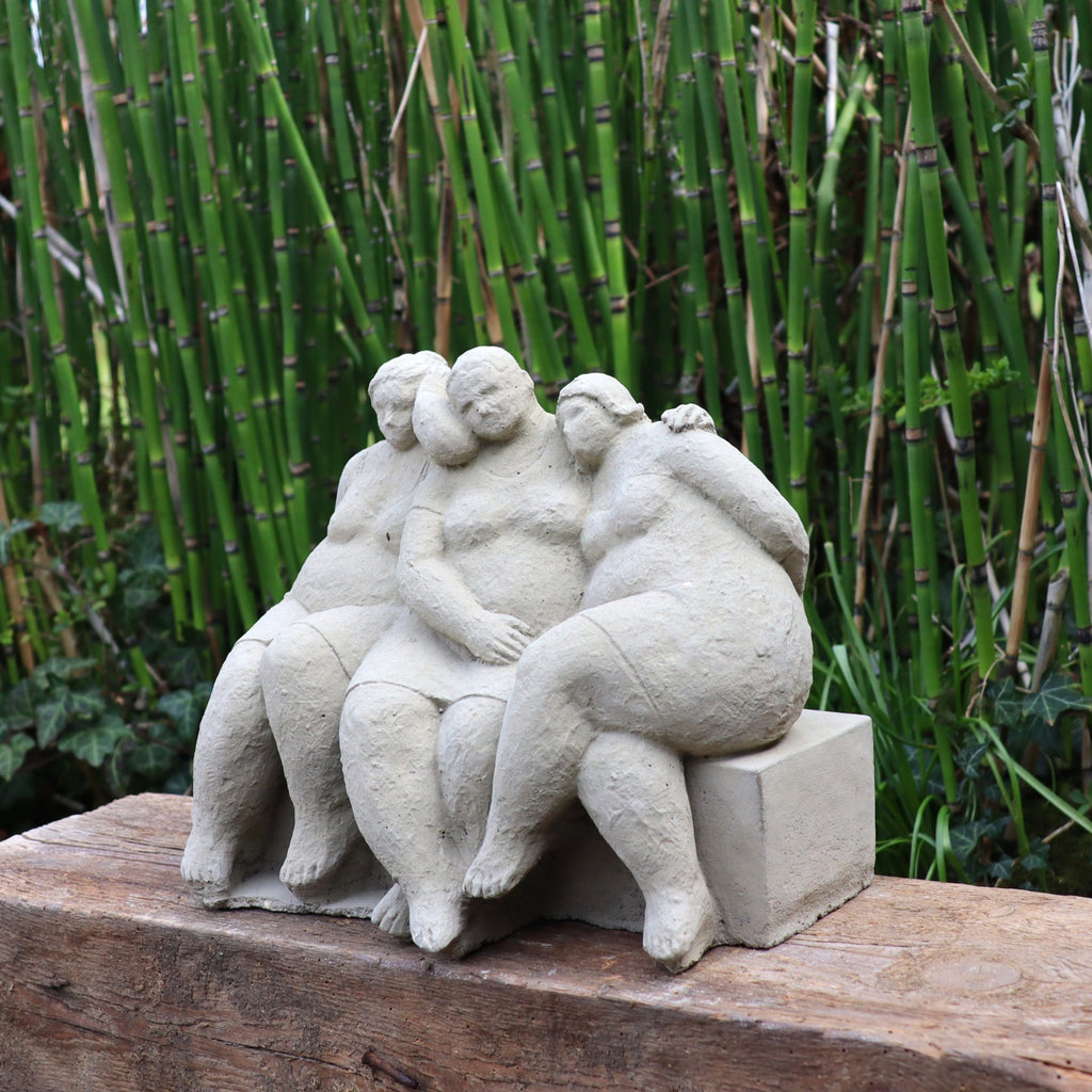 Die charmante Steinfigur "Freundschaft" für Ihren Garten zeigt drei sitzende Personen mit Armen umschlungen, handgefertigt in Deutschland aus hellem Stein - perfekt für echte Gartenliebe.