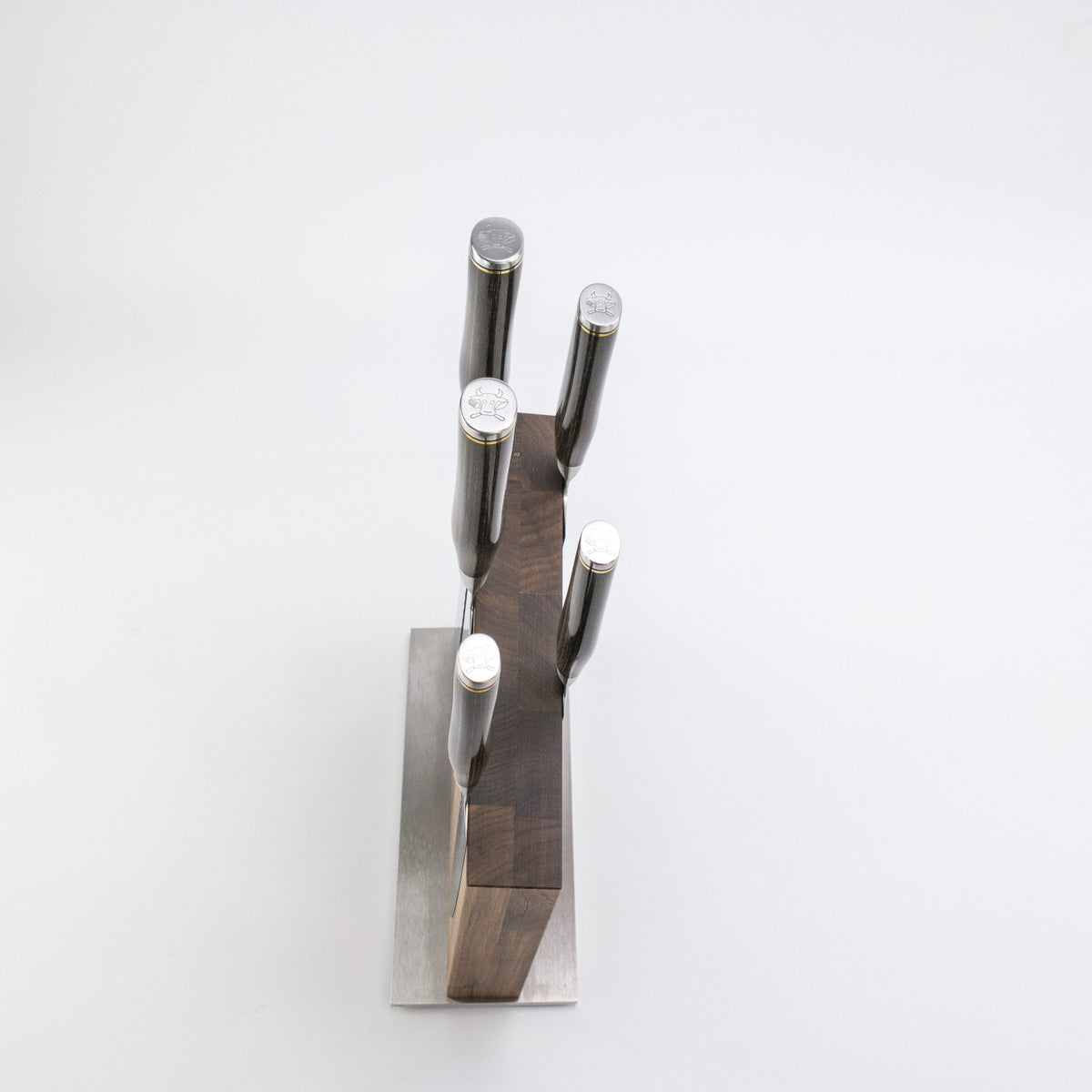 Eine Draufsicht auf das Exklusives Messerblock-Set - KAI Shun Tim Mälzer Damastmesser in einem hochwertigen Nussbaum-Magnet-Messerblock von Böker, angeordnet auf einem Metallsockel vor einem schlichten weißen Hintergrund.