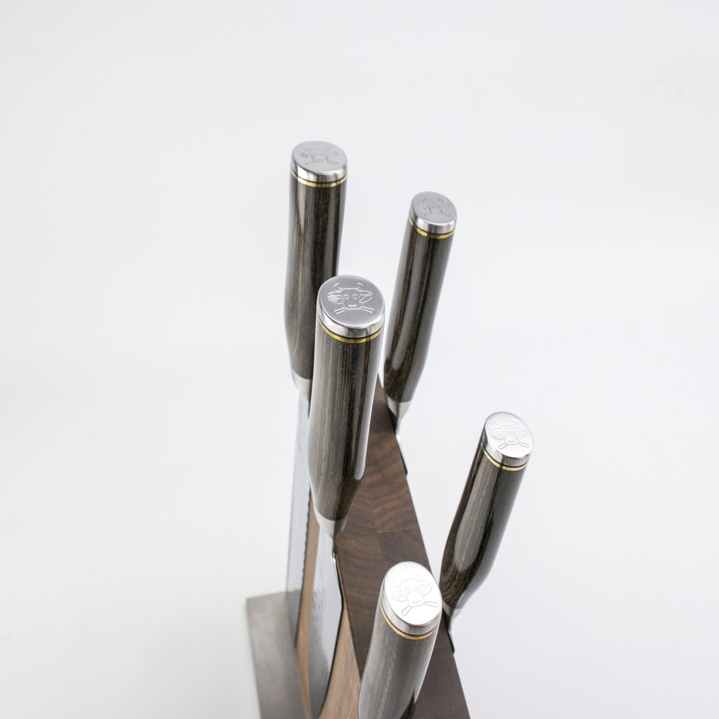 Das Exklusives Messerblock-Set - KAI Shun Tim Mälzer Damastmesser mit hochwertigem Magnet-Messerblock aus Walnuss von Böker präsentiert fünf Damastmesser mit graviertem Logo auf den Metall-Enden vor weißem Hintergrund.