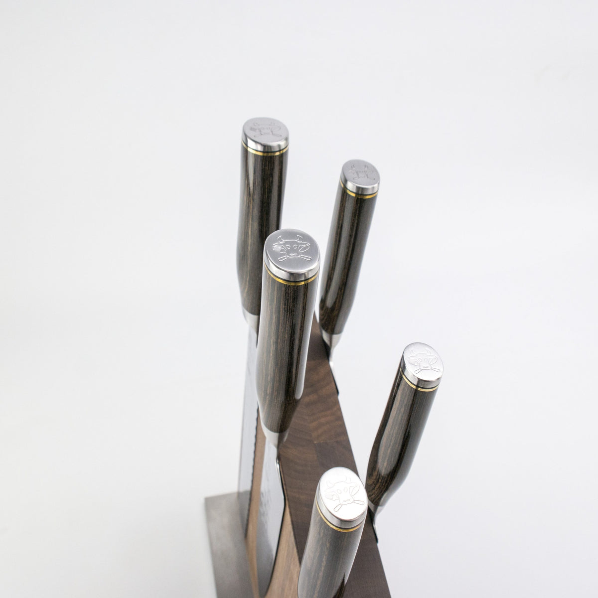 Das Exklusives Messerblock-Set - KAI Shun Tim Mälzer Damastmesser mit hochwertigem Magnet-Messerblock aus Walnuss von Böker präsentiert fünf Damastmesser mit graviertem Logo auf den Metall-Enden vor weißem Hintergrund.