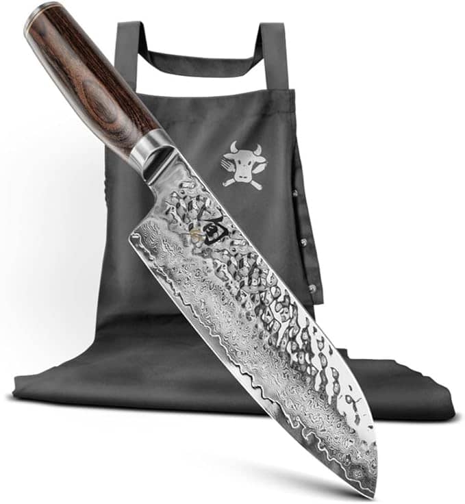 Ein Santokumesser mit Holzgriff wird mit einer schwarzen Kochschürze kombiniert, beides aus der KAI X-MAS SELECTION DREAMBOX. Die Santokuklinge weist die komplizierten Muster des Damaszenerstahls auf, ergänzt durch das minimalistische Stierlogo der Schürze, was sie zu einer exquisiten Ergänzung jeder festlichen Sammlung macht.