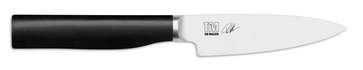 Wir präsentieren die KAI X-MAS SELECTION DREAMBOX Tim Mälzer Kamagata: ein elegantes Kochmesser mit schwarzem Griff und glänzender Klinge, auf deren Unterseite das Logo „TM Walker“ und die Signatur von Tim Mälzer Kamagata zu sehen sind. Dieses außergewöhnliche Messer ist ideal für jedes kulinarische Traum-Setup und hebt sich von seinem schlichten weißen Hintergrund ab.