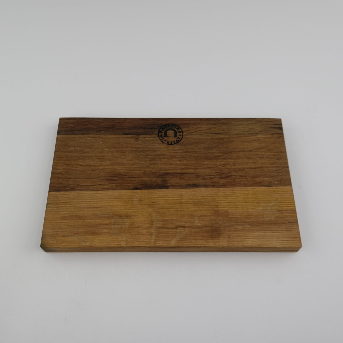 Ein rechteckiges Schneidebrett aus Holz aus dem Set Kai Shun Premier Tim Mälzer Minamo TMM-0701 zeigt zwei unterschiedliche Holztöne, mit einem dunkleren Braun oben und einem helleren unten. Ein kleines, rundes Kai Shun Premier-Logo ist nahe der oberen Mittelkante auf einem schlichten weißen Hintergrund aufgedruckt.