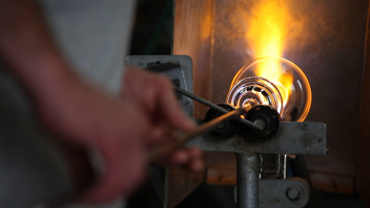Eine Person formt geschmolzenes Glas mit Metallwerkzeugen durch eine helle Flamme und demonstriert so die Glasbläserei zur Herstellung des Wasserglas "Side" VISION-Serie - 2er-Set | 480 ml Design-Gläser, exklusives Glas für Spirituosen.