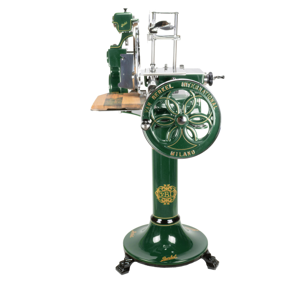 Der Berkel Volano B114 in Sonderlackierung British Racing Green ist ein mechanischer Allesschneider im Vintage-Stil, der mit aufwendigen Verzierungen verziert ist, darunter ein Rad mit Blumenmuster. Er trägt die Etiketten „Berkel Volano B114“ und „Milano“ und verfügt über eine Holzplattform für Lebensmittel sowie eine Schneidemessereinheit an der Oberseite.