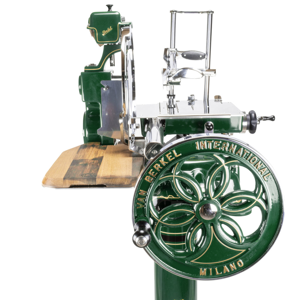 Ein Berkel Volano B114 Fleischschneider in Sonderlackierung British Racing Green, in einer atemberaubenden Kombination aus British Racing Green und Silber, steht auf einem Holzsockel. Er verfügt über einen großen runden Griff mit dekorativen Ausschnitten und komplizierten Metallkomponenten für präzises Fleischschneiden. Dieser manuelle Allesschneider mit der Marke „Berkel Internationals“ ist sowohl funktional als auch stilvoll.