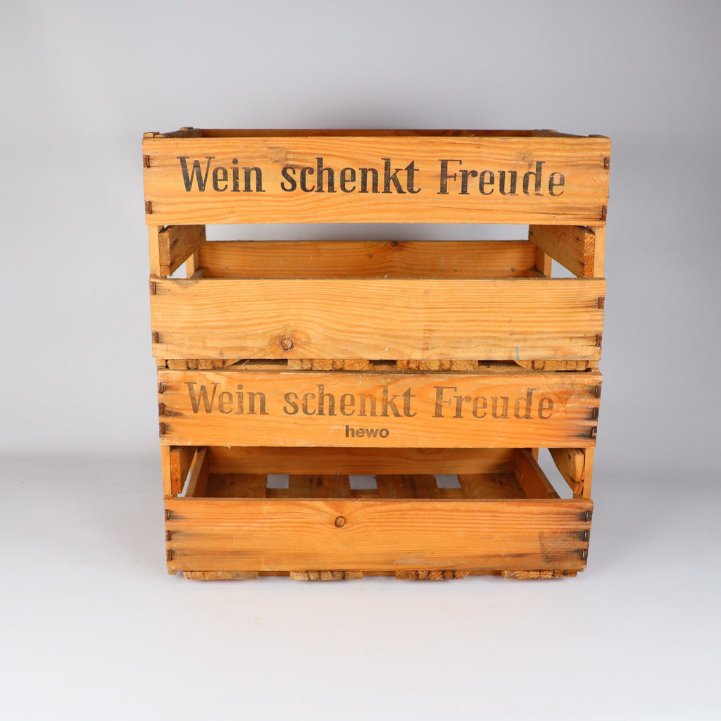Zwei alte Weinkisten der Marke Alte Weinkiste Holz aus der Pfalz sind gestapelt und tragen den Spruch „Wein schenkt Freude“. Die untere Kiste trägt die Aufschrift „hewo“. Sie stehen charmant auf einem makellos weißen Hintergrund.