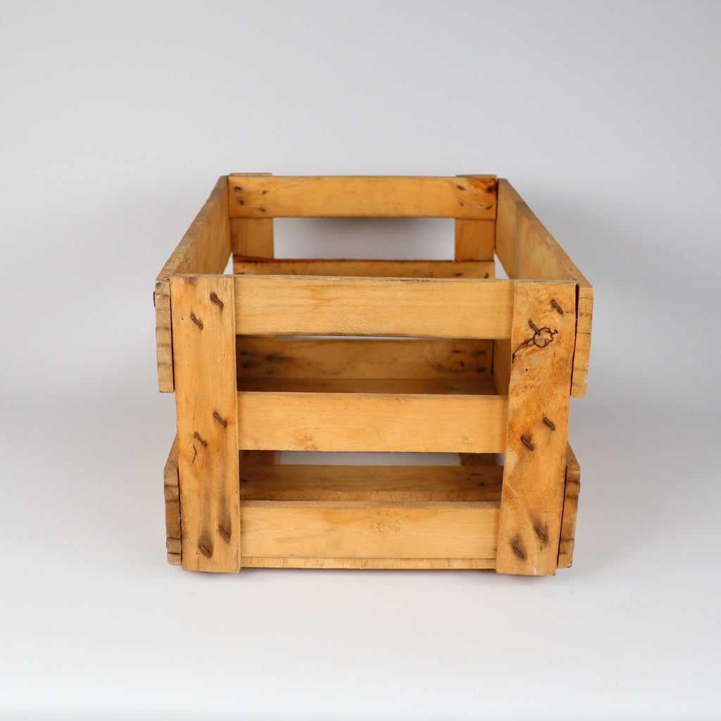 Eine Holzkiste mit natürlichem Finish wird vor einem schlichten weißen Hintergrund präsentiert. Die Kiste, die an eine Alte Weinkiste Holz Vintage aus der Pfalz mit Aufschrift erinnert, ist rechteckig, hat eine offene Oberseite und Lattenseiten und weist einige Gebrauchsspuren auf, was ihr ein rustikales Aussehen verleiht.
