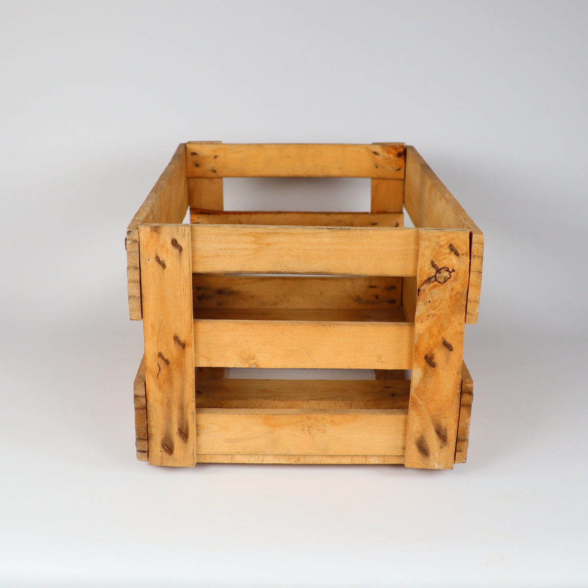 Eine Holzkiste mit natürlichem Finish wird vor einem schlichten weißen Hintergrund präsentiert. Die Kiste, die an eine Alte Weinkiste Holz Vintage aus der Pfalz mit Aufschrift erinnert, ist rechteckig, hat eine offene Oberseite und Lattenseiten und weist einige Gebrauchsspuren auf, was ihr ein rustikales Aussehen verleiht.