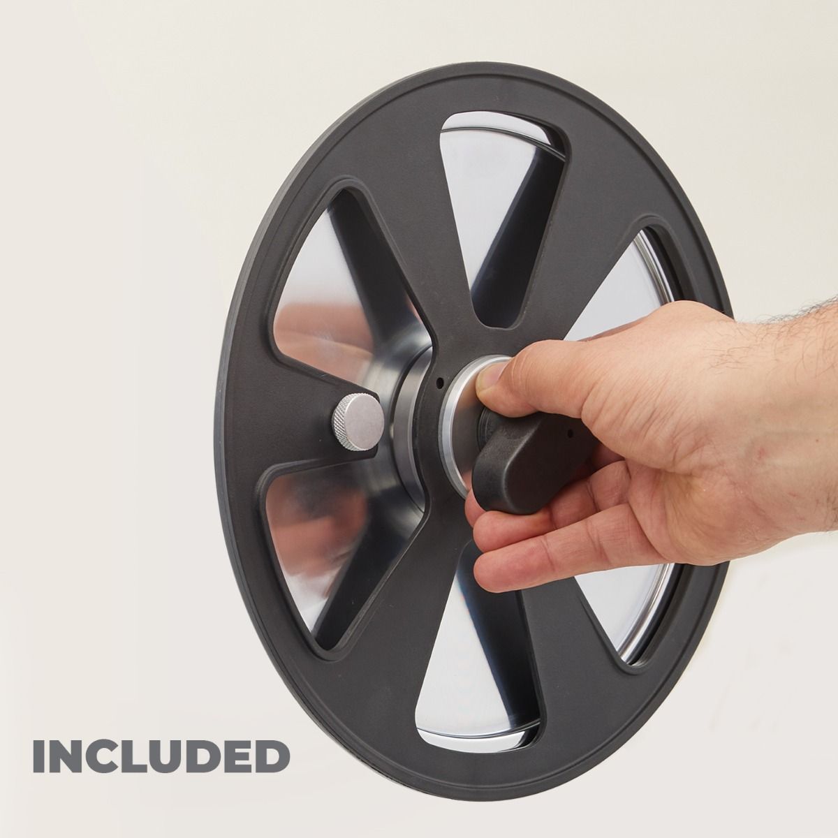 Eine Hand hält ein schwarzes Schwungrad für ein Spinbike mit einem zentralen Knopf. Das elegante Design weist vier ausgeschnittene Abschnitte und eine metallische Oberfläche auf, die an die Präzision des Wellenschliff-Messer-Bausatzes für Berkel Home Line 200/250 Plus erinnert. Das Wort „INKLUSIVE“ wird in grauer Schrift in der unteren linken Ecke angezeigt.