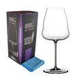 Ein klares Weißweinglas Riedel Winewings Sauvignon Blanc mit hohem Stiel steht neben einer violett-schwarzen Geschenkbox mit der Aufschrift „Riedel Winewings“. Vor der Box und dem Glas liegt ein gefaltetes blaues Poliertuch.