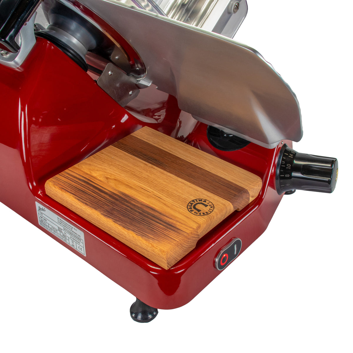 Bild einer Berkel Aufschnittmaschine Pro Line XS 25 Rot, Der Profi Allesschneider für Ihre Küche mit einem 100% handgefertigten Fassholzbrett-Unikat-Einsatz. Der Allesschneider verfügt über ein schwarzes Einstellrad und einen Netzschalter an der Seite. Das Schneidebrett verfügt über ein kleines rundes Logo mit einem Design in der Nähe einer Ecke. Der Profi Allesschneider steht vor einem weißen Hintergrund.