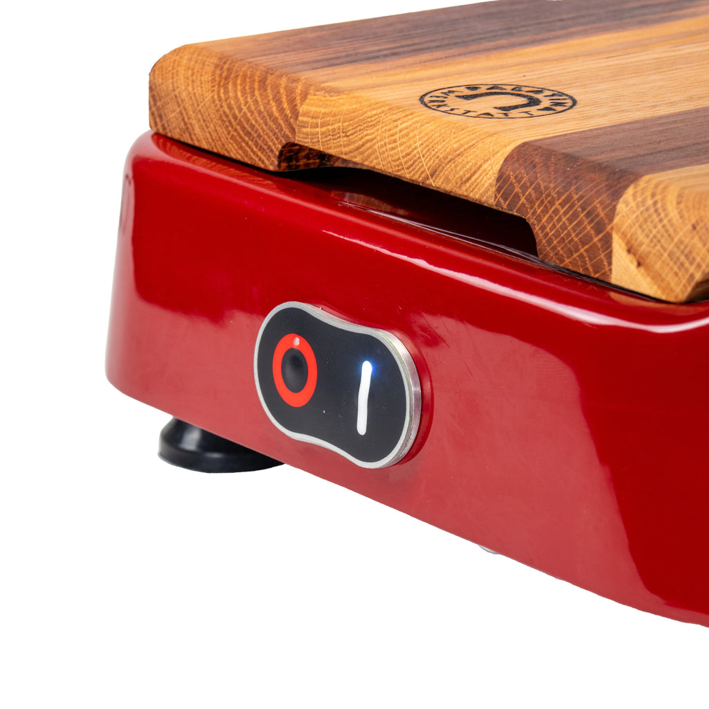 Nahaufnahme einer roten Berkel Aufschnittmaschine Pro Line XS 25, Der Profi Allesschneider für Ihre Küche, mit einem Ein-/Ausschalter. Das Gerät verfügt über ein 100 % handgefertigtes Fassholzbrett Unikat auf der Oberseite und einen schlanken, roten Metallsockel mit einem kleinen hervorstehenden Bedienknopf. Der Schalter ist teilweise beleuchtet und zeigt damit an, dass das Gerät eingeschaltet ist.