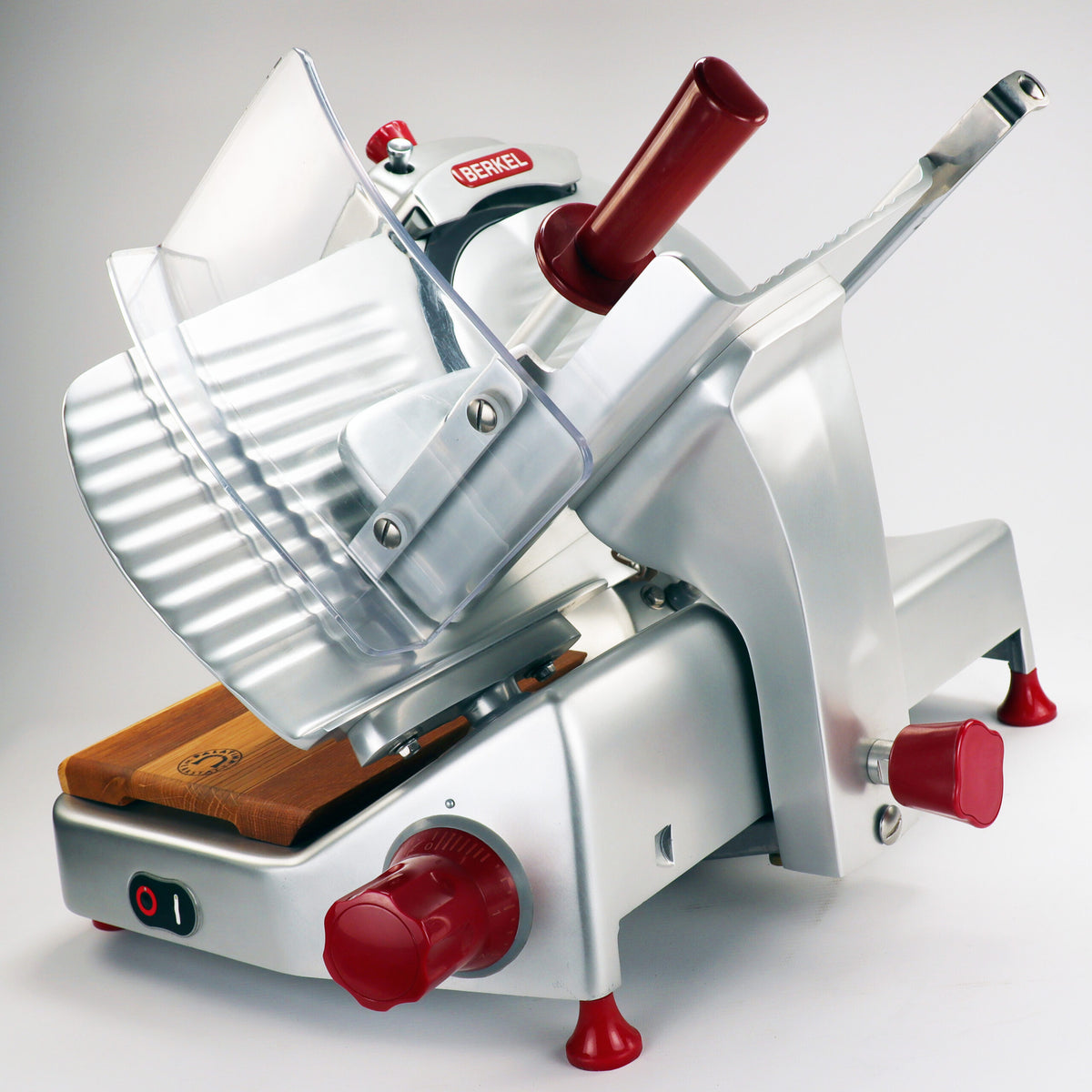 Ein silberner Berkel Pro Line XS 25, ein professioneller Aufschnittschneider mit rotem Akzent, verfügt über eine geneigte Klinge, einen Schutzschild und verschiedene Einstellknöpfe zum Schneiden von Fleisch und Käse. Dieser Schneider verfügt außerdem über eine Holzplattform aus Fassholz zum Platzieren der Lebensmittel und Gummifüße für Stabilität.