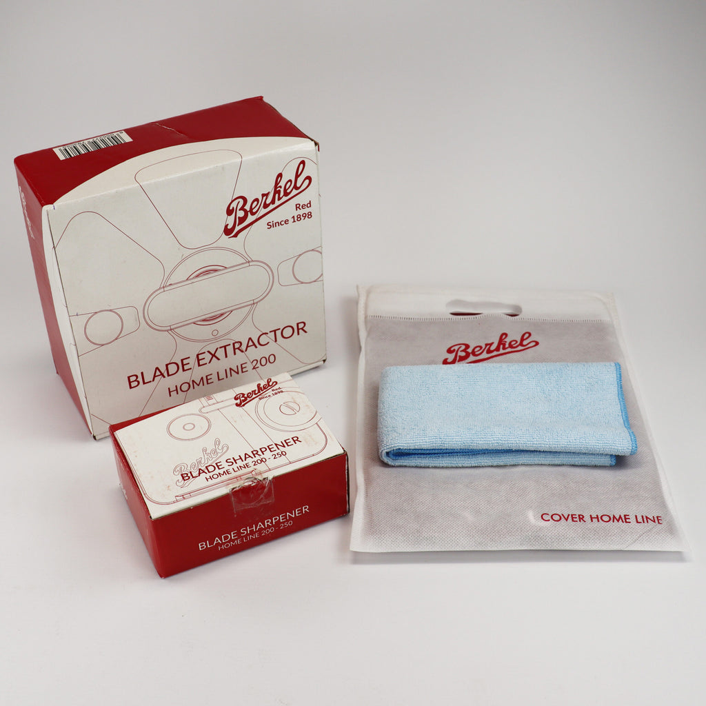Ein Set mit Küchenzubehör der Marke Berkel, genannt „Berkel Home Line 200 Zubehörset“, enthält einen verpackten Klingenabzieher, einen verpackten Schleifaufsatz und eine verpackte blaue Abdeckung. Auf der Verpackung jedes Artikels in diesem Set ist das Berkel-Logo deutlich sichtbar.