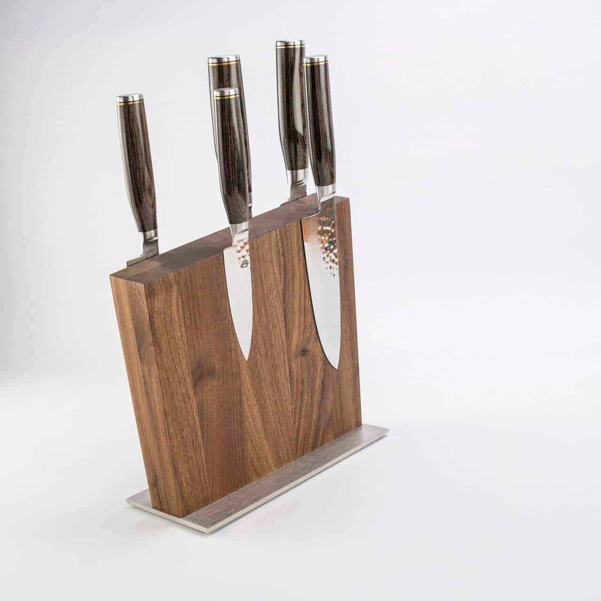 Ein Exklusives Messerblock-Set, KAI Shun Tim Mälzer Damastmesser mit einem hochwertigen magnetischen Messerblock von Böker, bestehend aus drei großen Messern und zwei kleineren Messern mit glatten, dunklen Griffen und polierten Edelstahlklingen, ist vor einem schlichten weißen Hintergrund positioniert.