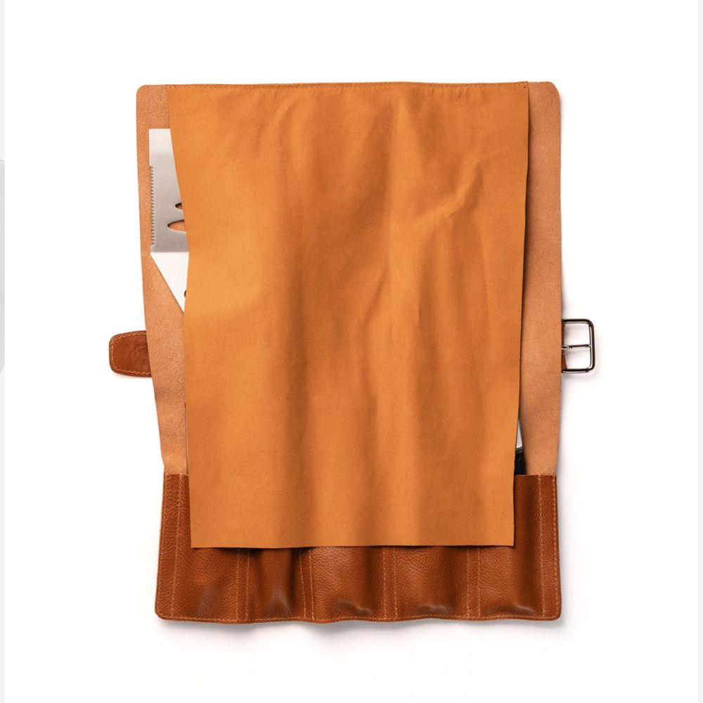 Die Berkel Messertasche - eine braune Ledertasche mit einer teilweise geöffneten Klappe - zeigt einen Notizblock und mehrere Fächer im Inneren, die vor einem weißen Hintergrund stehen.