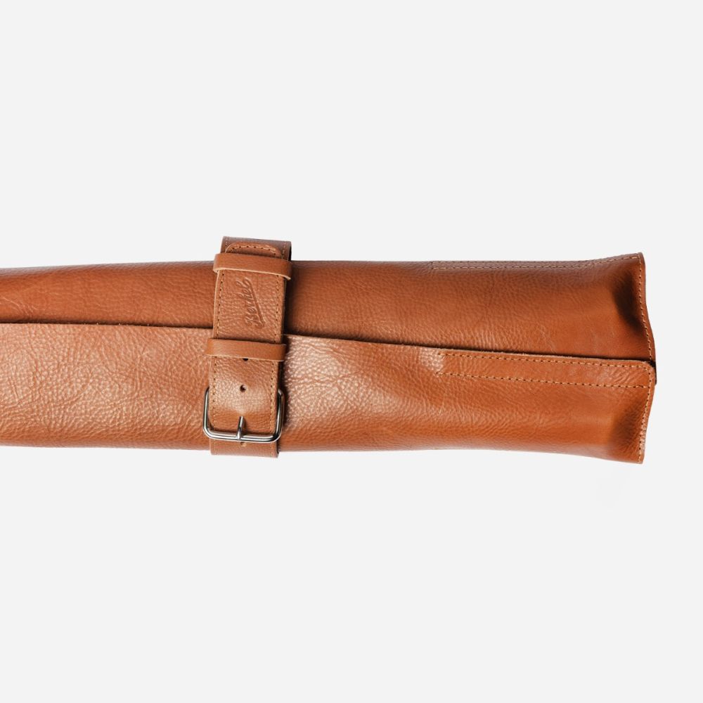 Die Berkel Messertasche ist eine aufgerollte hellbraune Ledertasche, die mit einem passenden Riemen und einer Metallschnalle gesichert ist.