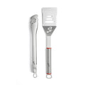 Das Berkel BBQ-Set, abgebildet auf weißem Hintergrund, umfasst eine Edelstahlzange und einen Pfannenwender - beide mit einer "B"-Aussparung und geschlungenen Griffen. Der Pfannenwender hat rote Griffakzente.