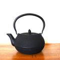 Eine handgefertigte schwarz-goldene Gusskanne aus Gusseisen mit strukturiertem, abgerundetem Griff steht elegant auf Holz vor einem weißen Hintergrund und spiegelt den Charme einer chinesischen Teekanne wider.