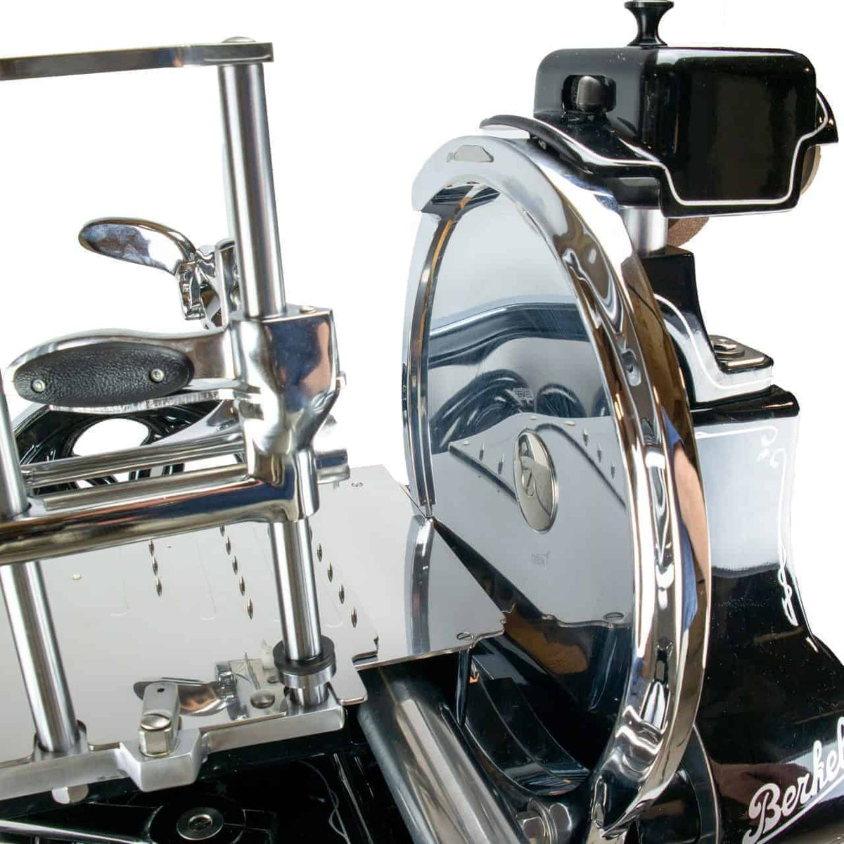 Eine antike Fleischschneidemaschine mit Handkurbel, glänzenden, verchromten Teilen und einem schwarzen Sockel. Die Maschine hat eine runde Schneide, einen Griff mit Griff und aufwendige Metalldetails. Der Markenname „Berkel“ ist auf der rechten Seite des Sockels zu sehen.