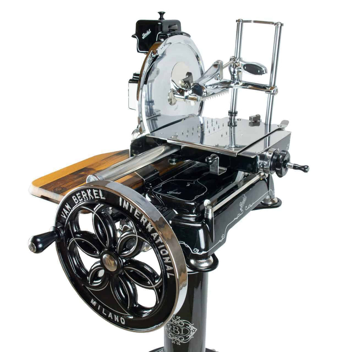 Eine handbetriebene Aufschnittmaschine im Vintage-Stil mit der Aufschrift „V.M. Berkel International Milano“ auf einem großen Schwungrad in Schwarz und Chrom. Das glänzende Chrommesser und die komplizierten mechanischen Teile des Berkel Volano B114 | schwarz sind deutlich zu sehen, und die manuelle Aufschnittmaschine ist zusammen mit einem Fassholzbrett auf einem Standfuß montiert.