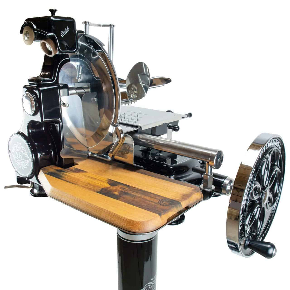 Der Berkel Volano B114, ein schwarzer manueller Fleischschneider im Vintage-Stil mit kunstvollen Verzierungen, verfügt über eine glänzende runde Klinge, polierte Metallteile, eine Holzplattform und ein Handkurbelrad. Sein Retro-Design hebt sich von einem weißen Hintergrund ab. Für zusätzliche Eleganz ist ein optionaler Standfuß erhältlich.