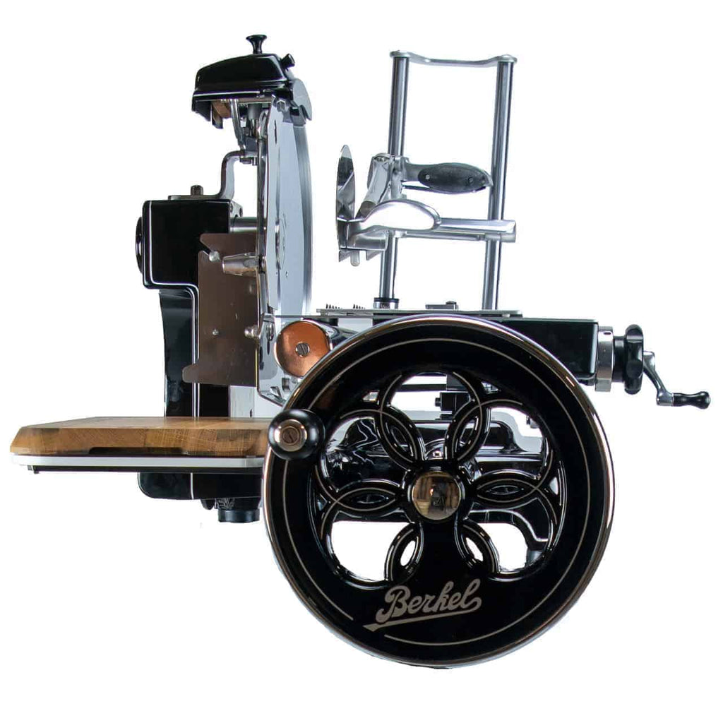 Die Berkel Volano B3 Schwarz Aufschnittmaschine mit Schwungrad verfügt über aufwendige, dekorative Metallarbeiten an der großen Handkurbel, eine polierte Metallklinge, eine Schneideplattform aus Fassholz und ein elegantes Schwarz-Chrom-Finish. Dieser Vintage-Fleischschneider kombiniert kunstvoll Funktionalität mit klassischem Design.