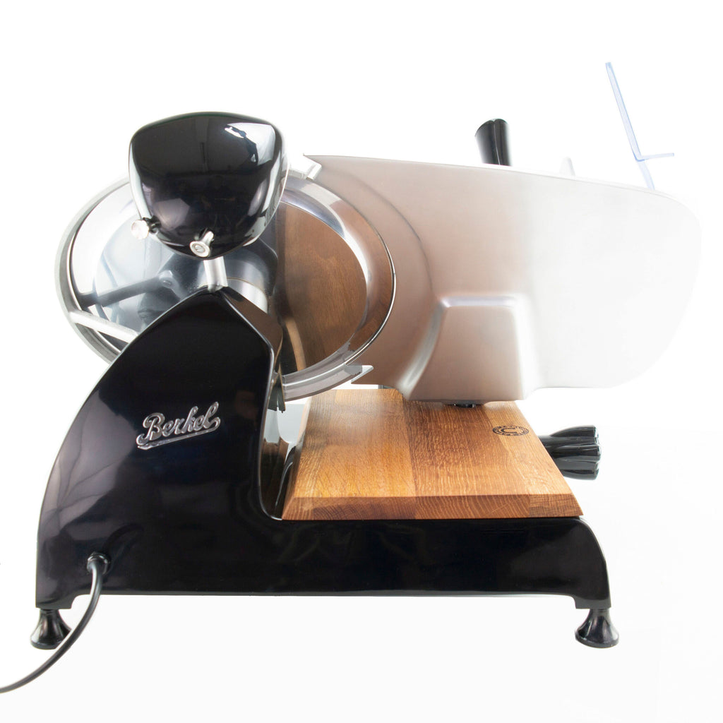 Eine elegante schwarz-weiße Berkel Red Line 300 Schwarz, Original Profi-Aufschnittmaschine mit glänzendem silbernem Messerdurchmesser 300 mm und hölzerner Fassholz-Einlegebrett-Schneidefläche. Die Profi-Aufschnittmaschine ist eingesteckt und ruht auf vier kleinen Füßen. Der Markenname „Berkel“ ist auf der Seite der Aufschnittmaschine auf weißem Hintergrund sichtbar.