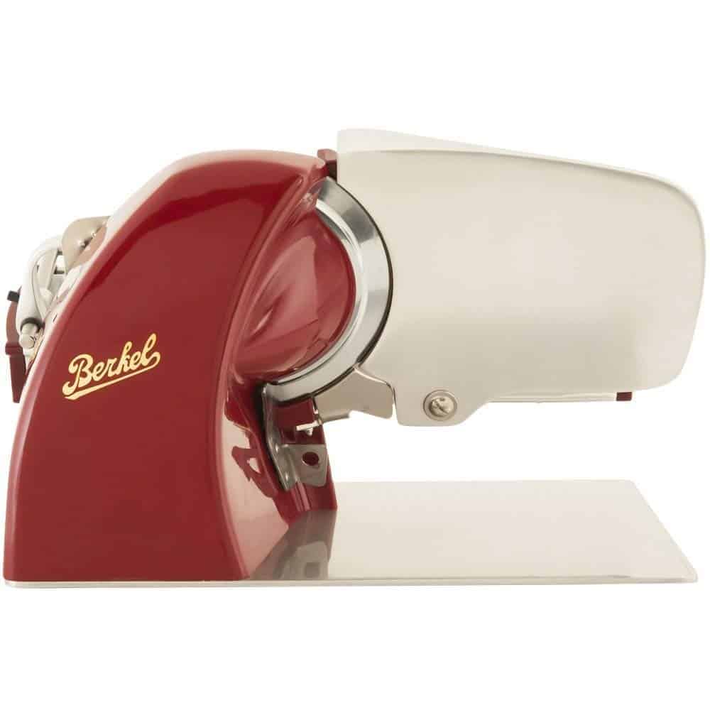 Ein roter Berkel-Fleischschneider aus Edelstahl im Seitenprofil. Der Schneider hat ein markantes rotes Motorgehäuse mit dem gelben „Berkel“-Logo und eine glänzende Klingenabdeckung aus Edelstahl. Das Gerät steht auf einem flachen, reflektierenden Sockel.