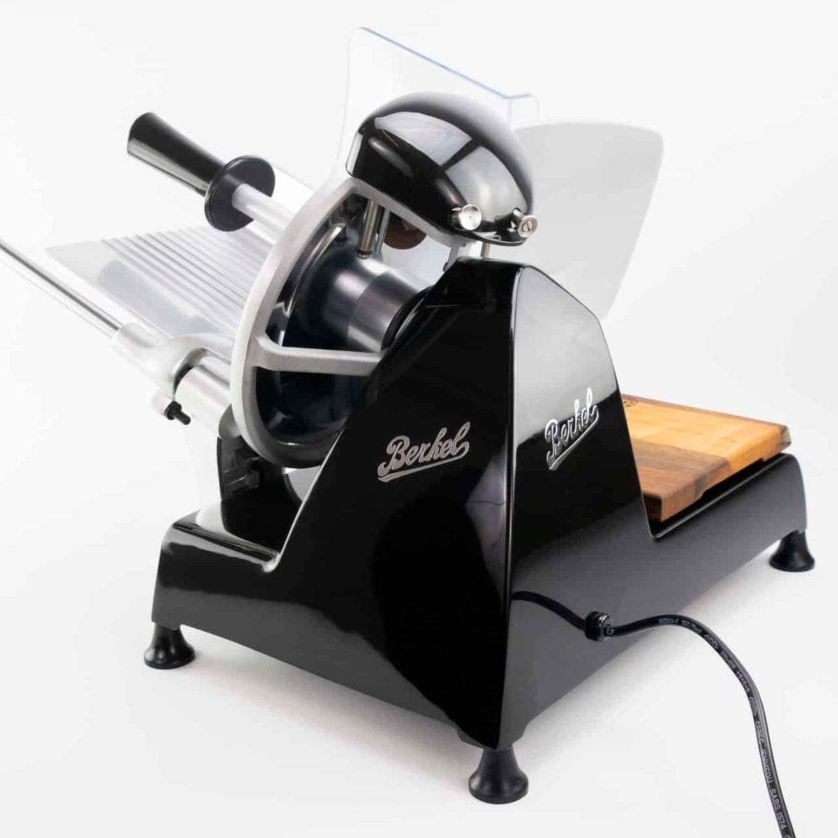 Eine schwarze Berkel-Aufschnittmaschine ist in einer Seitenansicht vor einem schlichten weißen Hintergrund zu sehen. Die Maschine hat eine glänzende Oberfläche, einen Griff, ein rundes Messer und auf der rechten Seite eine Holzschale zum Auffangen der geschnittenen Lebensmittel. Das Netzkabel ist an der Basis sichtbar.