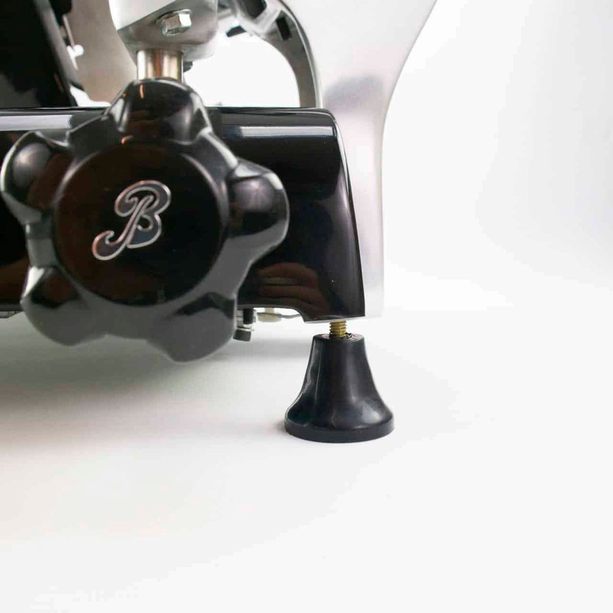 Eine Nahaufnahme des verstellbaren Fußes eines mechanischen Geräts mit einem schwarzen Knopf und dem eingravierten Buchstaben „B“. Der Fuß scheint Teil einer größeren Maschine zu sein, mit weißem Hintergrund.
