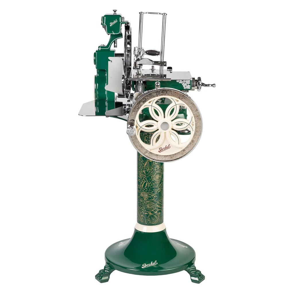 Das Berkel Volano B114 Sondermodell Schwungradmaschine incl. Standfuß + Fassholzbrett hat ein grün-silbernes Vintage-Design, ein verziertes Rad mit Blumenmuster, Emaille- und Metallakzente und steht auf einem passenden dekorativen Sockel.