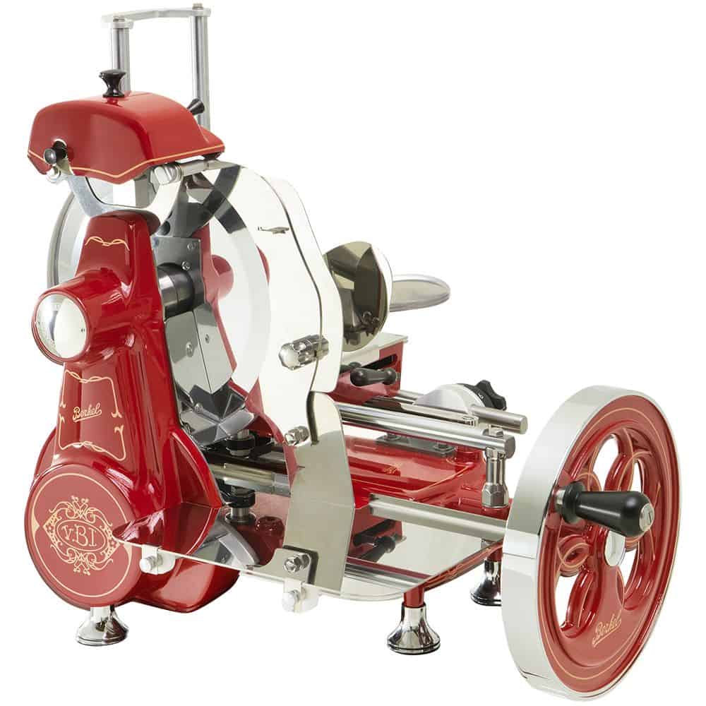 Das Bild zeigt eine Aufschnittmaschine mit Handkurbel im Vintage-Stil in Rot und Chrom, die an die Berkel Volano B2 Rot erinnert, Schwungradmaschine - Wunderschöne Aufschnittmaschine + Fassholzbrett Unikat. Diese Aufschnittmaschine verfügt über ein großes, rundes Schneidrad und aufwendige Details, darunter ein dekoratives Emblem auf der Basis. Die Aufschnittmaschine ist für präzises Schneiden von Fleisch konzipiert.