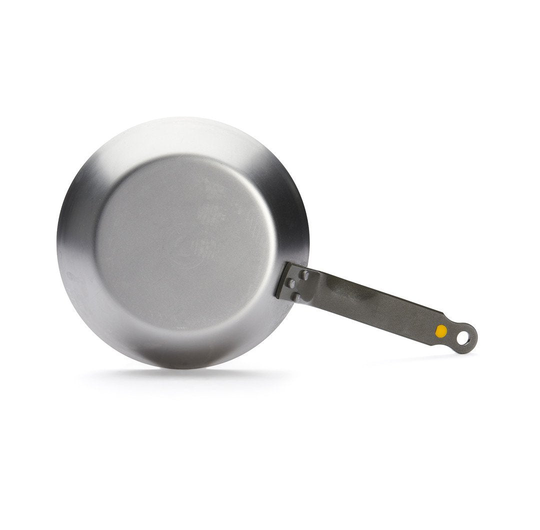 Die De Buyer Bratpfanne Mineral B aus Edelstahl wird von oben gezeigt - sie hat einen flachen Boden, einen langen Metallgriff mit gelbem Akzent am Ende und eignet sich ideal zum scharfen Anbraten.