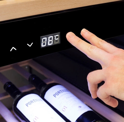 Nahaufnahme einer Person, die die Temperatur auf einer digitalen Anzeige eines Weinkühlschranks 2 Zonen CASO WineComfort 38 Schwarz einstellt. Der mit Holzregalen ausgestattete Kühlschrank zeigt eine Temperatur von 8,8 °C an. Auf dem Regal unter dem Display sind drei „Portilio“-Weinflaschen zu sehen, die in diesem Weinkühlschrank mit zwei Zonen perfekt gelagert sind.