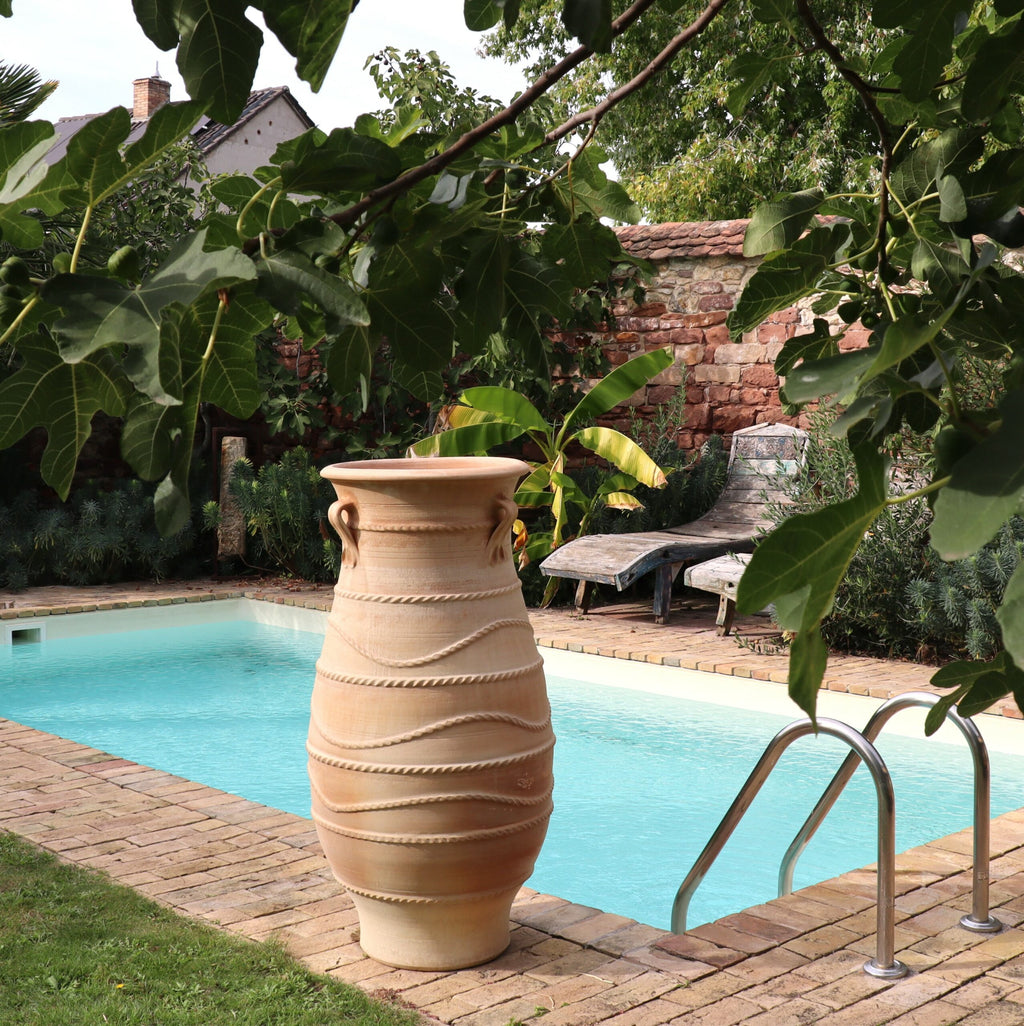 Ein ruhiger Pool im Hinterhof, umgeben von einer gemauerten Terrasse, verfügt über eine große, dekorative frostbeständige griechische Amphorenvase „Cistus“ H=1,30 m. Liegestühle stehen in der Nähe, und grüne Blattpflanzen und Cistus bilden eine üppige Kulisse und schaffen eine friedliche Gartenumgebung.